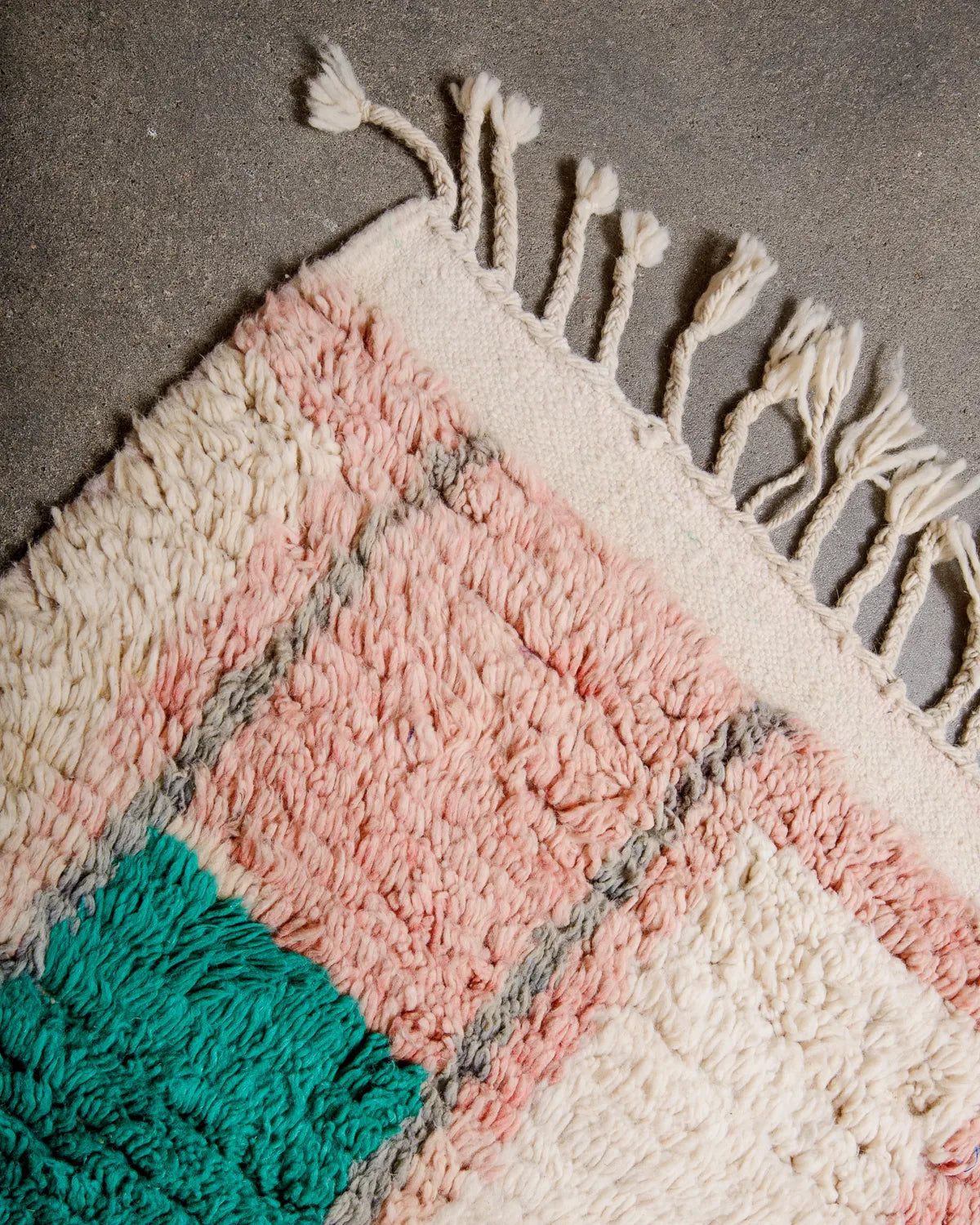 Tasseled edge of vintage wool rug laying on concrete floor.